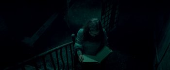 Movie still from “Scary Stories to Tell in the Dark” (2019), directed by André Øvredal – A woman sitting in a chair reading a book; Medium shot, High angle
