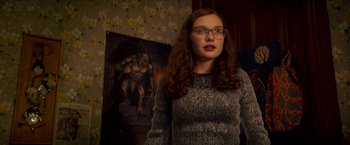 Movie still from “Scary Stories to Tell in the Dark” (2019), directed by André Øvredal – A woman with glasses standing in front of a painting; Medium shot, Over the shoulder angle