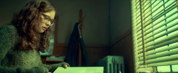 Movie still from “Scary Stories to Tell in the Dark” (2019), directed by André Øvredal – A man sitting at a table reading a book in front of an electric heater; Medium shot, Over the shoulder angle