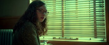 Movie still from “Scary Stories to Tell in the Dark” (2019), directed by André Øvredal – A woman wearing glasses sitting in front of a window; Medium shot, Low angle