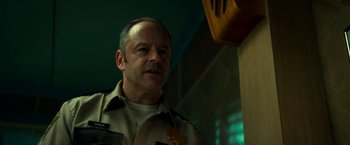 Movie still from “Scary Stories to Tell in the Dark” (2019), directed by André Øvredal – A man in a police uniform standing next to a wall; Close Up shot, Low angle