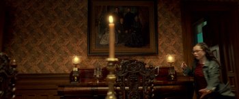 Movie still from “Scary Stories to Tell in the Dark” (2019), directed by André Øvredal – A candle lit in front of a painting of a family portrait; Wide shot, Low angle