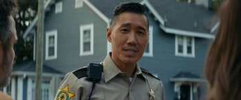 Movie still from “Scream” (2022), directed by Matt Bettinelli-Olpin – A man in a police uniform is standing in front of a house; Close Up shot, Low angle