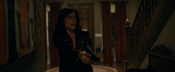 Movie still from “Scream” (2022), directed by Matt Bettinelli-Olpin – A woman holding a gun while standing in a living room; Medium shot, Over the shoulder angle