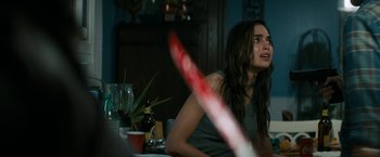 Movie still from “Scream” (2022), directed by Matt Bettinelli-Olpin – A woman sitting at a dining room table holding a red object; Close Up shot, Over the shoulder angle