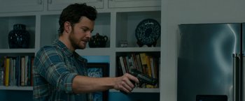 Movie still from “Scream” (2022), directed by Matt Bettinelli-Olpin – A man holding a gun in a room with shelves; Close Up shot, Over the shoulder angle
