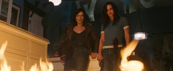 Movie still from “Scream” (2022), directed by Matt Bettinelli-Olpin – A couple of women standing next to each other holding hands; Medium shot, High angle