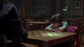 Movie still from “Searching for Bobby Fischer” (1993), directed by Steven Zaillian – A boy sitting at a table with his arms folded over his head; Close Up shot, Over the shoulder angle