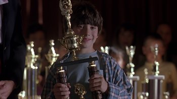 Movie still from “Searching for Bobby Fischer” (1993), directed by Steven Zaillian – A young boy holding a trophy in front of a group of people; Close Up shot, Low angle