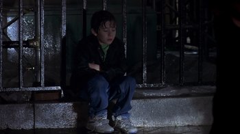 Movie still from “Searching for Bobby Fischer” (1993), directed by Steven Zaillian – A boy sitting on the ground next to a railing at night; Medium shot, Low angle