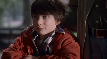 Movie still from “Searching for Bobby Fischer” (1993), directed by Steven Zaillian – A young boy sitting in a chair with his arms folded on his chest; Close Up shot, Over the shoulder angle