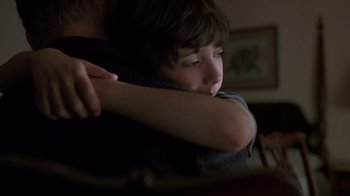 Movie still from “Searching for Bobby Fischer” (1993), directed by Steven Zaillian – A young boy hugging his father in a dark room; Close Up shot, Over the shoulder angle