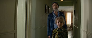 Movie still from “Seberg” (2019), directed by Benedict Andrews – A man standing next to a young boy in a room; Medium shot, Over the shoulder angle