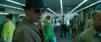 Movie still from “Seberg” (2019), directed by Benedict Andrews – A man wearing a hat and sunglasses while standing next to a crowd of people; Medium shot, Low angle