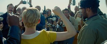 Movie still from “Seberg” (2019), directed by Benedict Andrews – A person raising their hand in front of a crowd of onlookers; Medium shot, Low angle