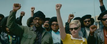 Movie still from “Seberg” (2019), directed by Benedict Andrews – A group of people standing next to each other holding their hands up in the air; Medium shot, Low angle