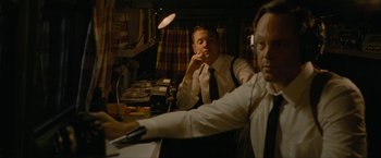 Movie still from “Seberg” (2019), directed by Benedict Andrews – Two men sitting at a table in front of a microphone; Medium shot, Low angle