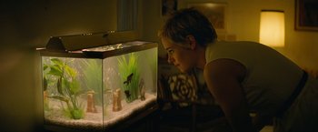 Movie still from “Seberg” (2019), directed by Benedict Andrews – A woman looking at a fish tank in a living room; Medium shot, High angle