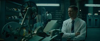 Movie still from “Seberg” (2019), directed by Benedict Andrews – A man sitting in front of a computer in a room; Medium shot, Low angle