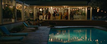 Movie still from “Seberg” (2019), directed by Benedict Andrews – A group of people standing around a pool at night; Extreme Wide shot, High angle