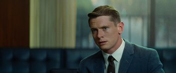 Movie still from “Seberg” (2019), directed by Benedict Andrews – A man wearing a suit and tie in front of a window; Close Up shot, Over the shoulder angle