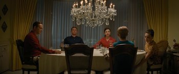 Movie still from “Seberg” (2019), directed by Benedict Andrews – A group of people sitting at a table in front of chandeliers; Wide shot, High angle