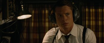 Movie still from “Seberg” (2019), directed by Benedict Andrews – A man wearing a tie and headphones looking at the camera; Close Up shot, Low angle