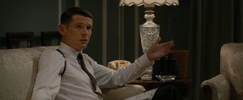 Movie still from “Seberg” (2019), directed by Benedict Andrews – A man sitting in front of a table with a lamp on it; Medium shot, Low angle