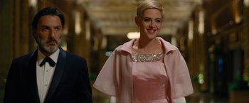 Movie still from “Seberg” (2019), directed by Benedict Andrews – A woman in a pink dress smiling for the camera; Medium shot, Over the shoulder angle