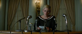Movie still from “Seberg” (2019), directed by Benedict Andrews – A person sitting at a table with microphones; Medium shot, Low angle