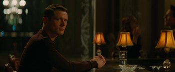 Movie still from “Seberg” (2019), directed by Benedict Andrews – A man sitting at a table in front of two lamps; Medium shot, Over the shoulder angle