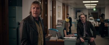 Movie still from “Official Secrets” (2019), directed by Gavin Hood – A man standing next to a desk in an office; Medium shot, Over the shoulder angle