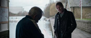 Movie still from “Official Secrets” (2019), directed by Gavin Hood – Two men standing next to each other near a body of water; Medium shot, Over the shoulder angle