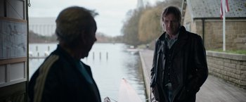 Movie still from “Official Secrets” (2019), directed by Gavin Hood – A man standing next to another man on a boat; Medium shot, Over the shoulder angle