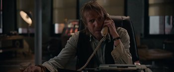 Movie still from “Official Secrets” (2019), directed by Gavin Hood – A man sitting at a desk talking on a phone; Medium shot, Over the shoulder angle