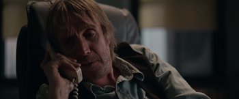 Movie still from “Official Secrets” (2019), directed by Gavin Hood – A man sitting on a chair talking on a phone; Close Up shot, Over the shoulder angle