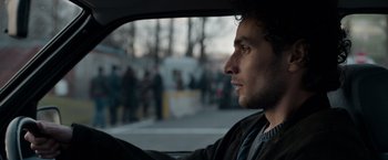 Movie still from “Official Secrets” (2019), directed by Gavin Hood – A man sitting in the driver's seat of a car looking out the window; Close Up shot, Over the shoulder angle