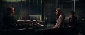 Movie still from “Official Secrets” (2019), directed by Gavin Hood – A woman sitting in front of a stack of papers; Medium shot, Over the shoulder angle