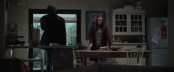 Movie still from “Official Secrets” (2019), directed by Gavin Hood – A woman standing at a dining room table in front of a bowl of fruit; Medium shot, Over the shoulder angle