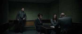 Movie still from “Official Secrets” (2019), directed by Gavin Hood – A group of people sitting at a table in a room; Wide shot, Over the shoulder angle