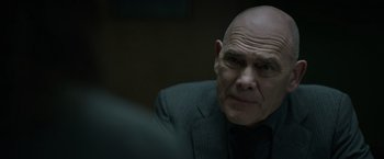 Movie still from “Official Secrets” (2019), directed by Gavin Hood – A bald man in a suit stares into the camera; Close Up shot, Over the shoulder angle