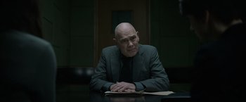 Movie still from “Official Secrets” (2019), directed by Gavin Hood – A man sitting at a table in front of a book; Medium shot, Over the shoulder angle