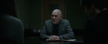 Movie still from “Official Secrets” (2019), directed by Gavin Hood – A bald man sitting at a table in a suit; Medium shot, Over the shoulder angle