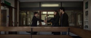 Movie still from “Official Secrets” (2019), directed by Gavin Hood – Two women and a man shake hands at a counter; Wide shot, Over the shoulder angle