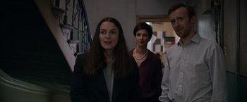 Movie still from “Official Secrets” (2019), directed by Gavin Hood – A group of people standing next to each other in a room; Medium shot, Over the shoulder angle