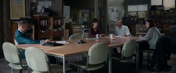 Movie still from “Official Secrets” (2019), directed by Gavin Hood – A group of people sitting at a table in an office; Wide shot, High angle