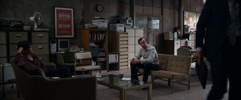 Movie still from “Official Secrets” (2019), directed by Gavin Hood – A man sitting on a couch in a room with papers on the floor; Wide shot, High angle