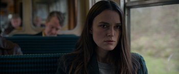 Movie still from “Official Secrets” (2019), directed by Gavin Hood – A woman sitting on a train looking at the camera; Close Up shot, Over the shoulder angle
