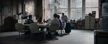 Movie still from “Official Secrets” (2019), directed by Gavin Hood – A group of people sitting at a table in front of a window; Wide shot, Over the shoulder angle