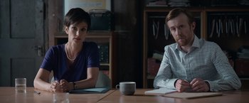 Movie still from “Official Secrets” (2019), directed by Gavin Hood – Two people sitting at a table with a cup of coffee; Medium shot, Over the shoulder angle
